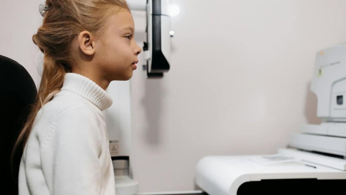 A young girl sits attentively during an eye examination with modern medical equipment.