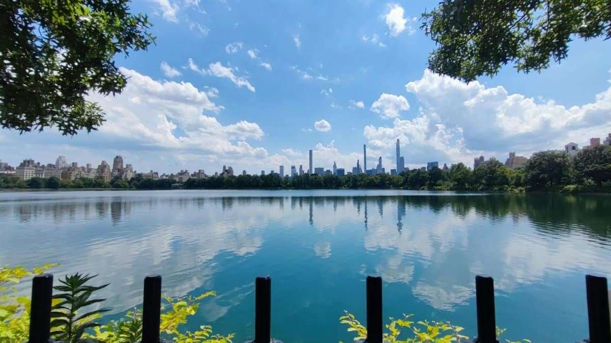 Beautiful view of Central Park's lake reflecting New York City's iconic skyline on a sunny day.