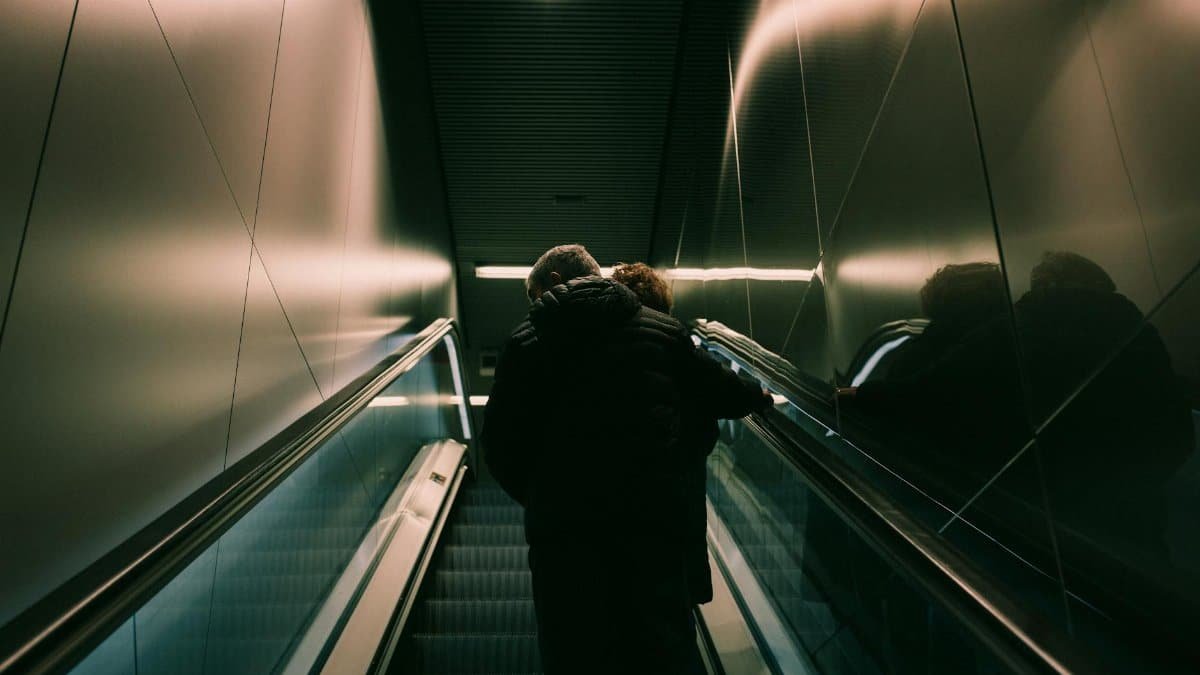 A couple embracing while riding an escalator indoors, reflecting urban intimacy.