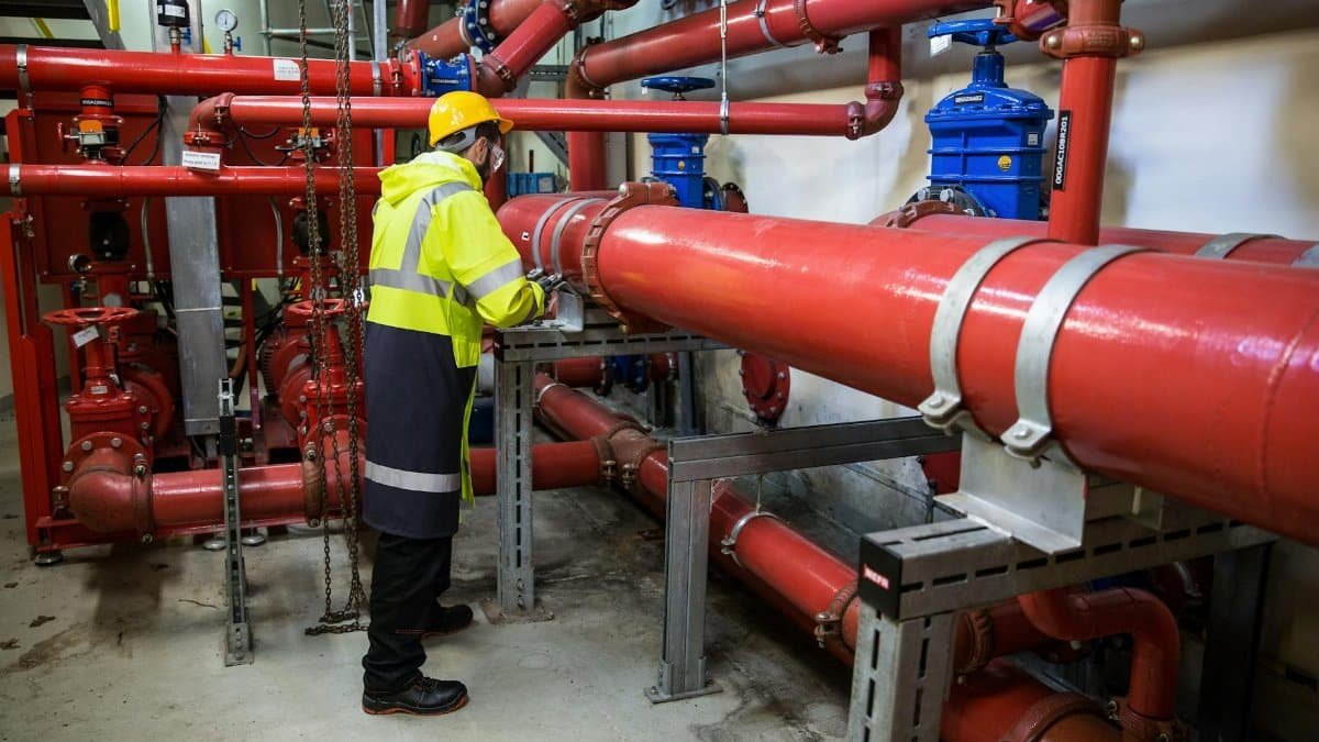 Engineer with safety gear inspecting red industrial piping system indoors.