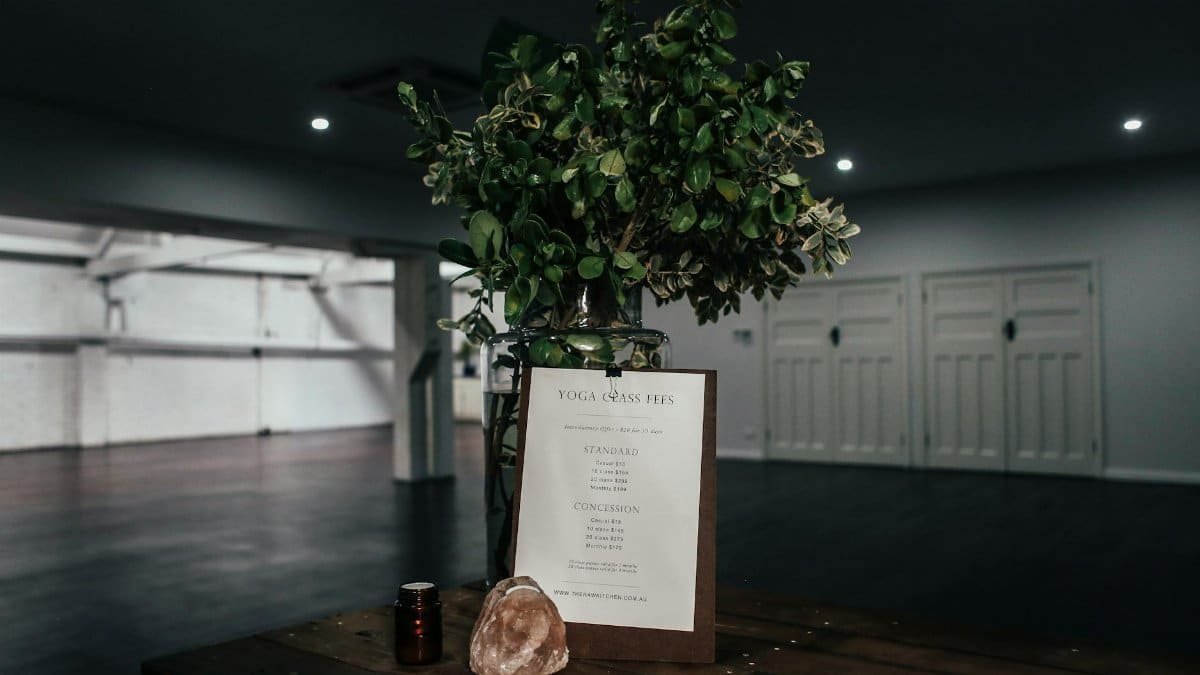 A tranquil yoga studio interior featuring a fee chart, decorative plant, and soft lighting.