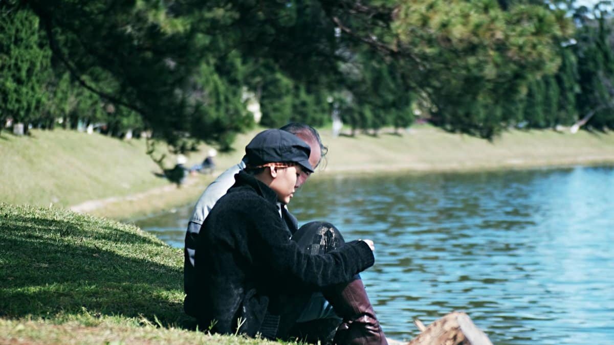 Two adults sitting by a lakeside, enjoying a peaceful day outdoors in a verdant park.