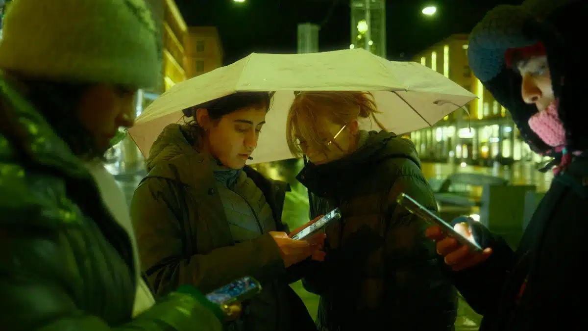 Group of friends using smartphones under an umbrella at night.