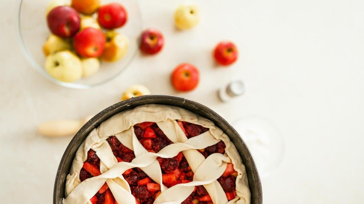 Fresh apple cherry pie ready to bake, paired with colorful apples.