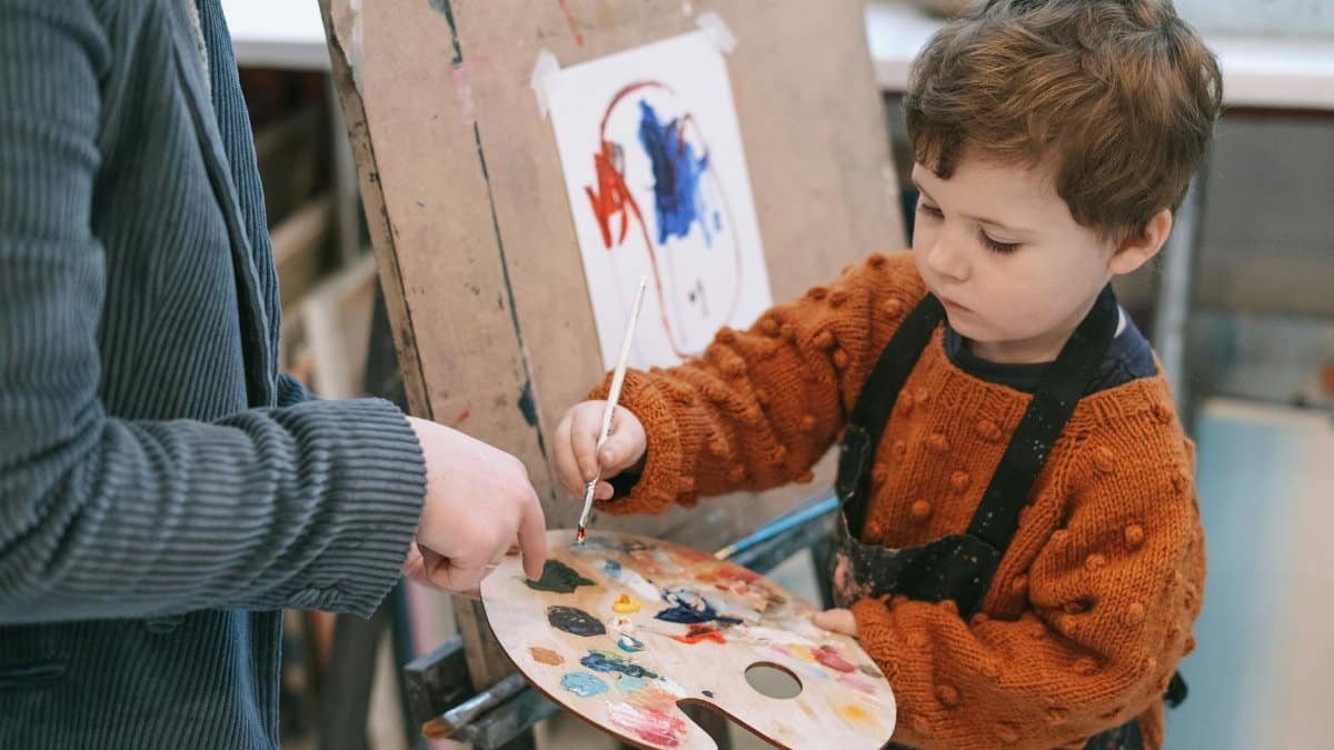 Young boy learning to paint with teacher's guidance during art class.