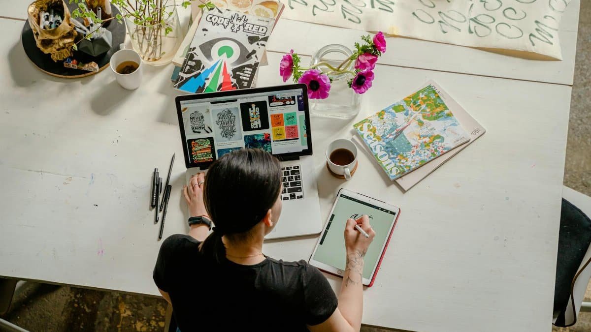 Artistic workspace featuring calligraphy and digital design on a tablet and laptop.
