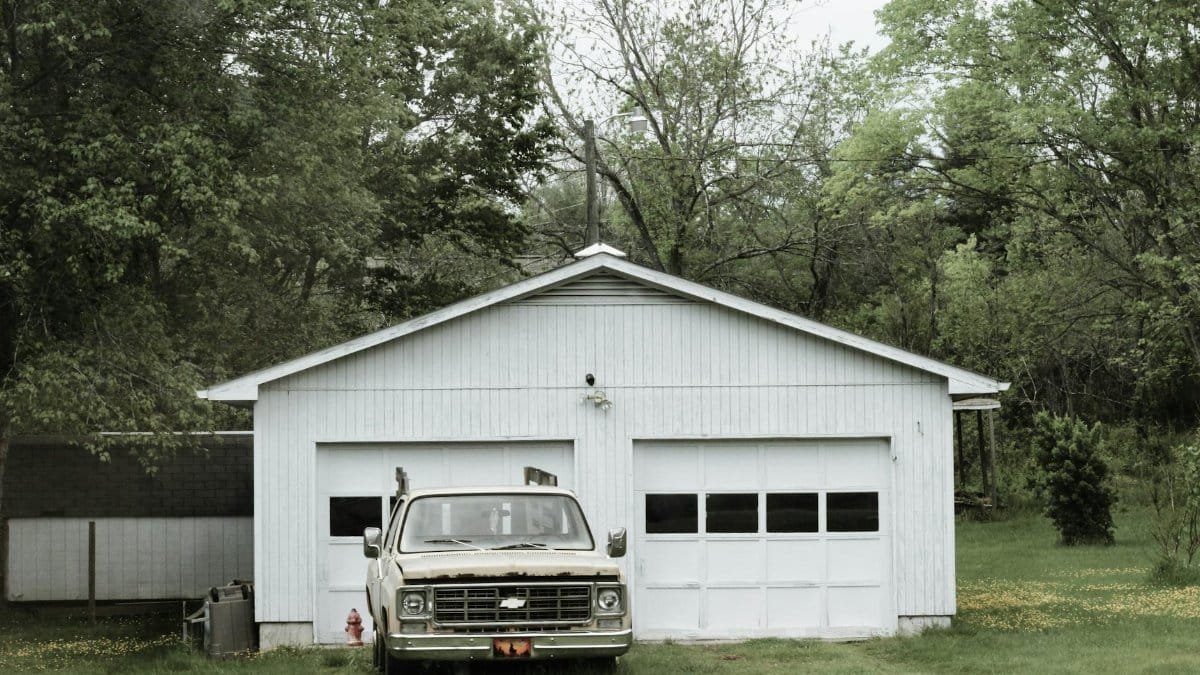 A classic pickup truck parked outside a wooden garage surrounded by lush greenery in Asheville, NC.