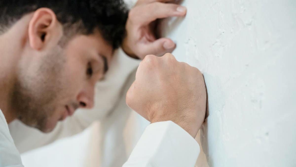 A man in distress leans on a white wall, depicting stress and anxiety.