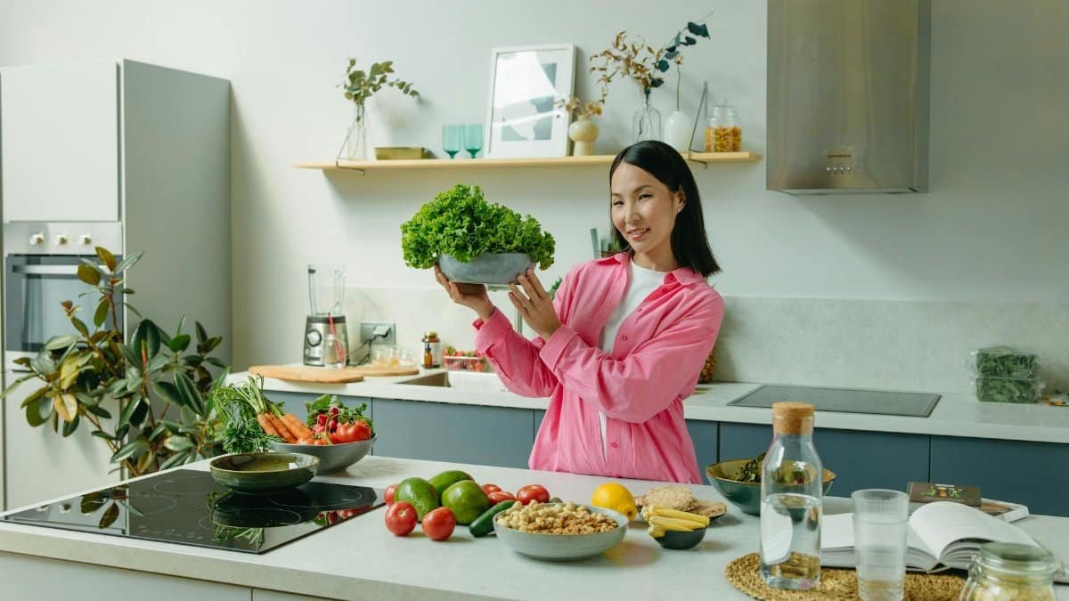 Woman in a kitchen holding fresh lettuce, surrounded by healthy ingredients like tomatoes and avocados, promoting healthy eating.