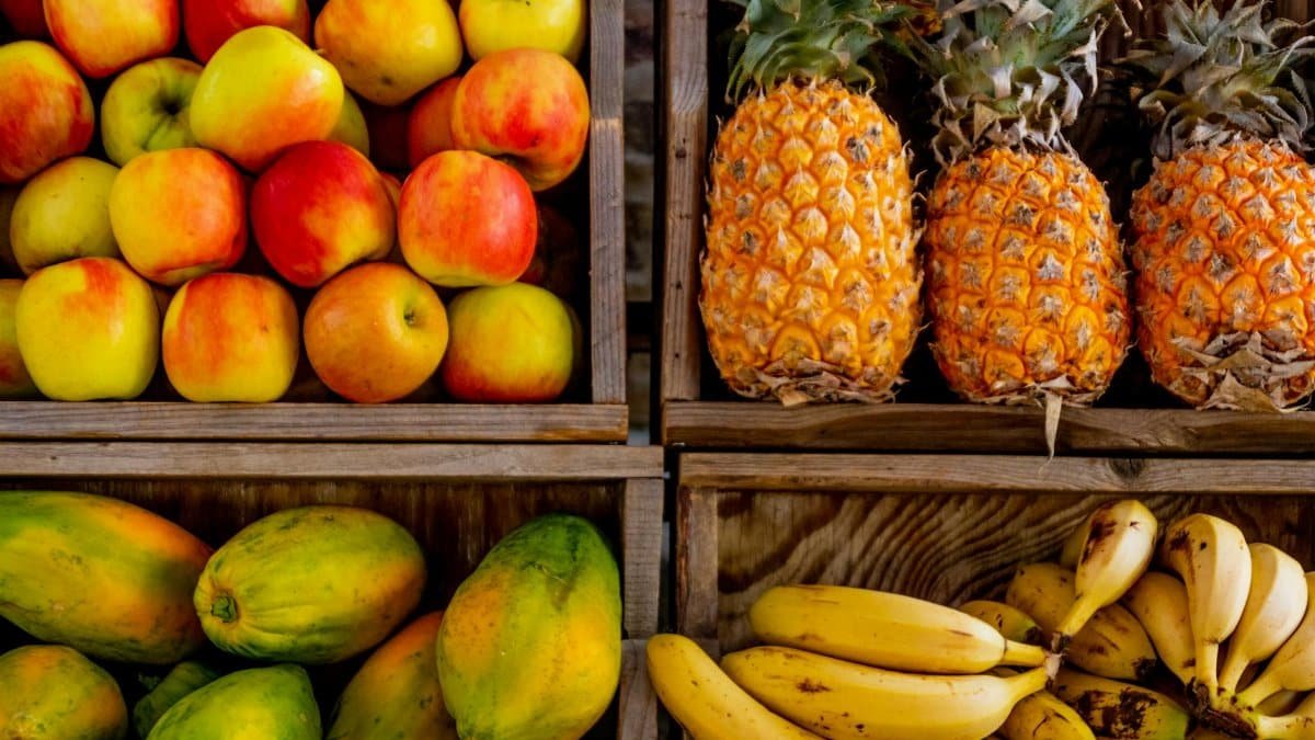 Colorful display of apples, pineapples, bananas, and papayas in wooden crates at a market.