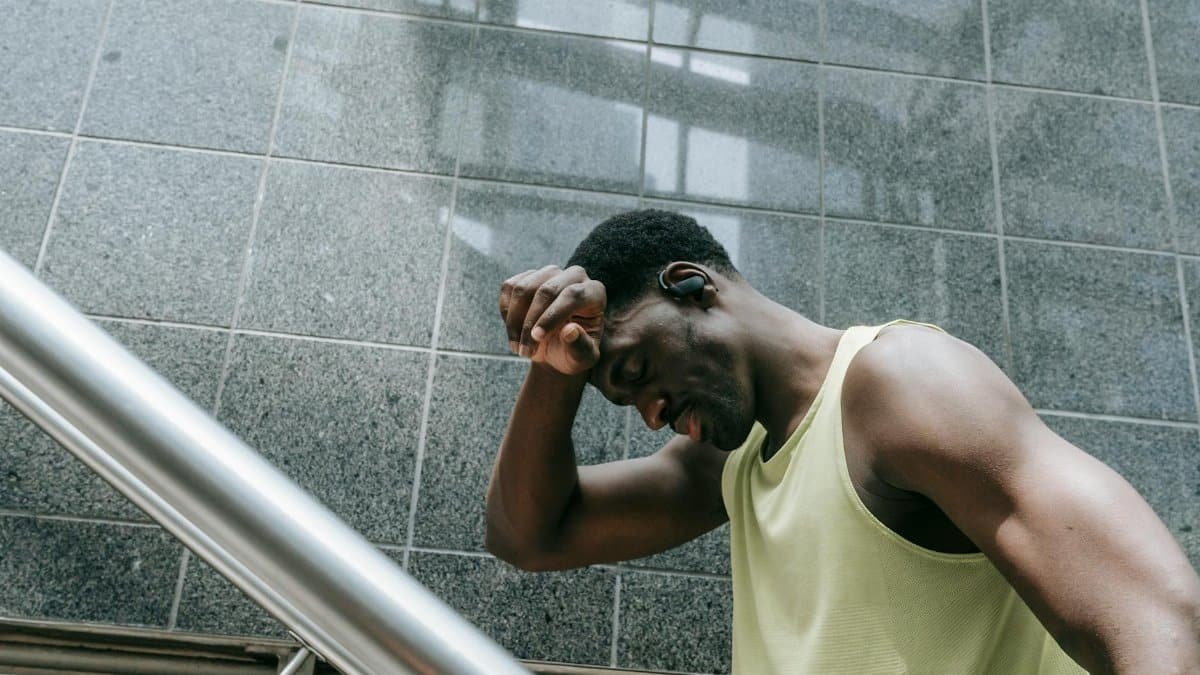 A tired black man resting on stairs in a modern building, reflecting fatigue and effort.