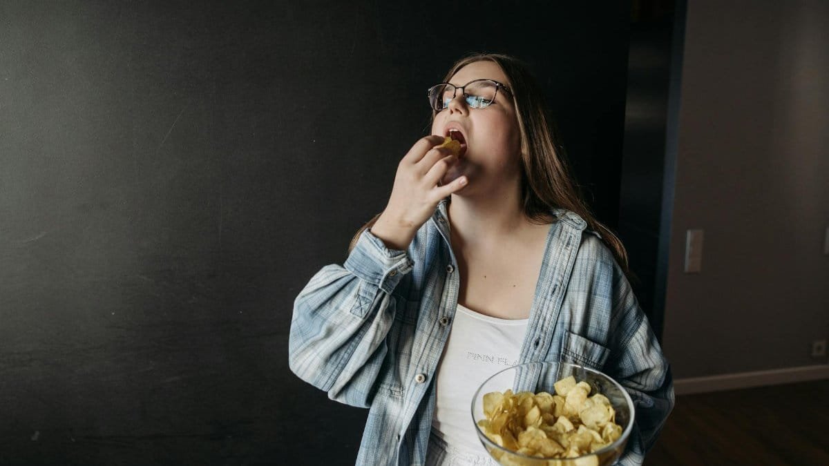 Young woman eating potato chips indoors, enjoying a snack moment.