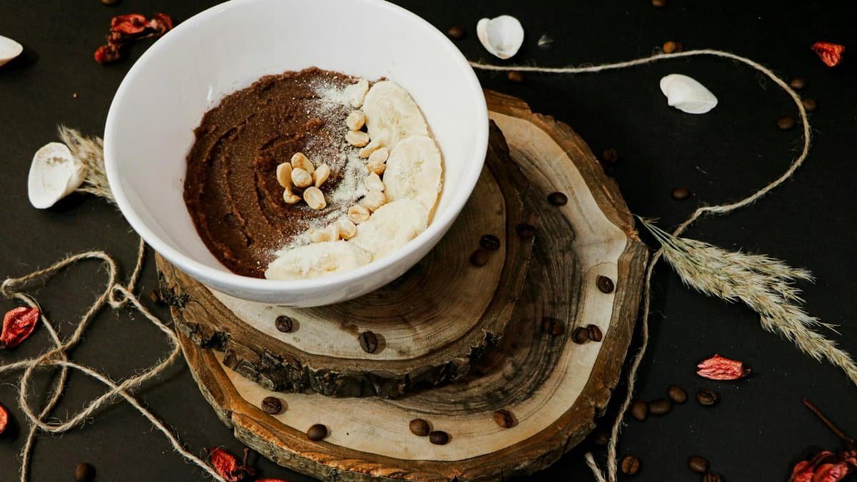 Top-down view of a chocolate smoothie bowl garnished with banana slices and nuts on rustic wood surface.