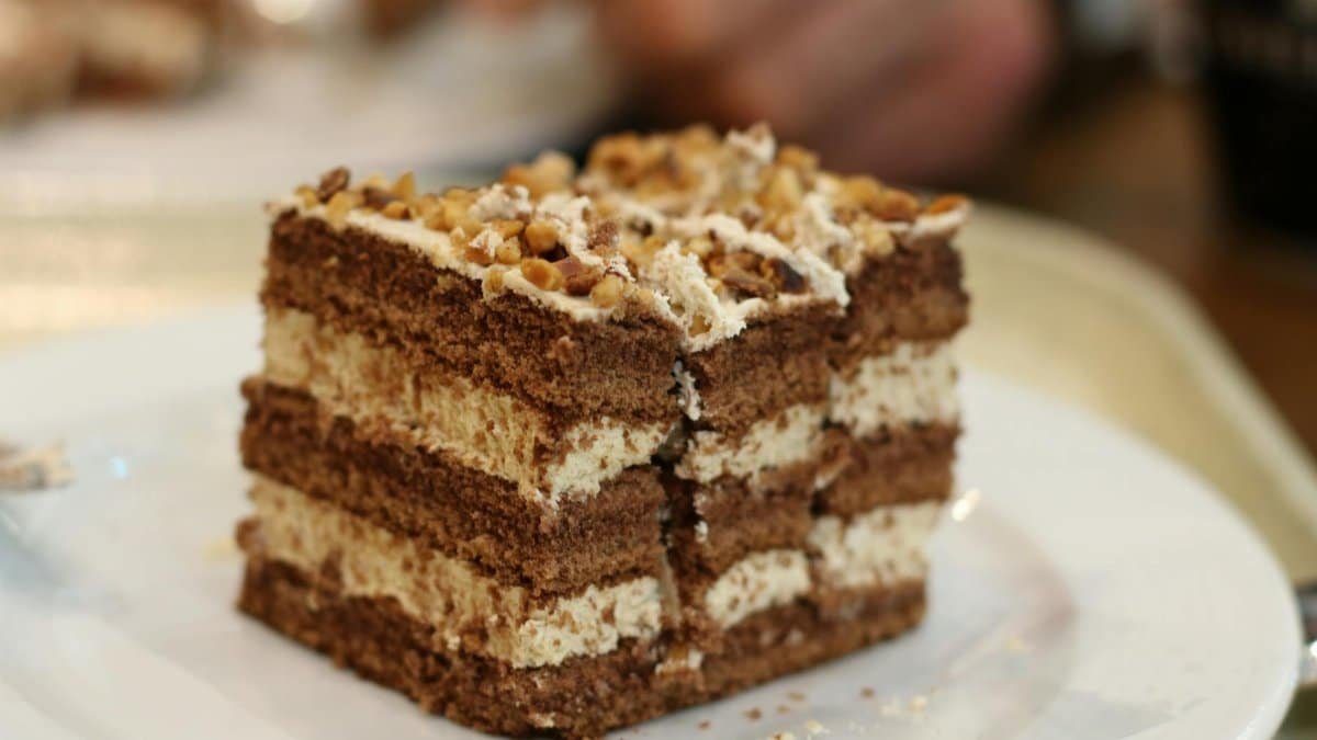 Close-up of a decadent coffee and walnut layered cake slice on a plate.
