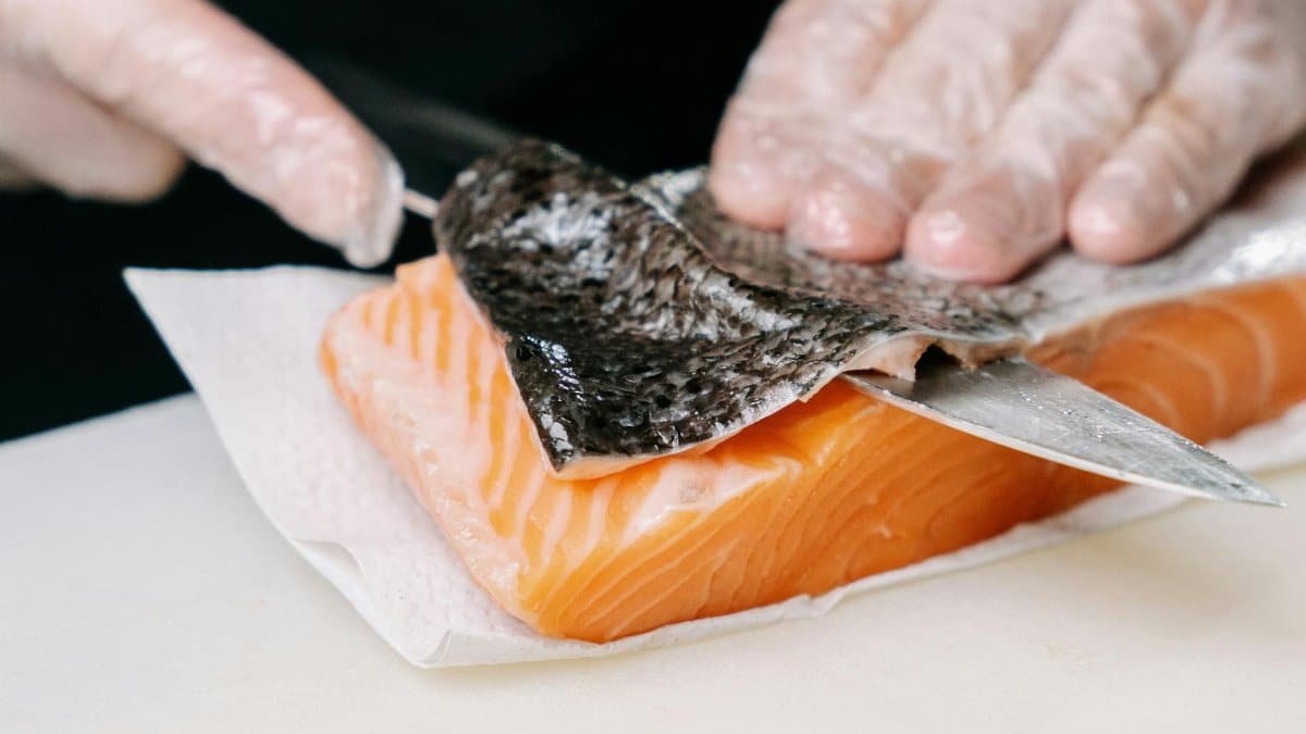 Close-up of salmon skin being removed by hands with a knife, showcasing food preparation.