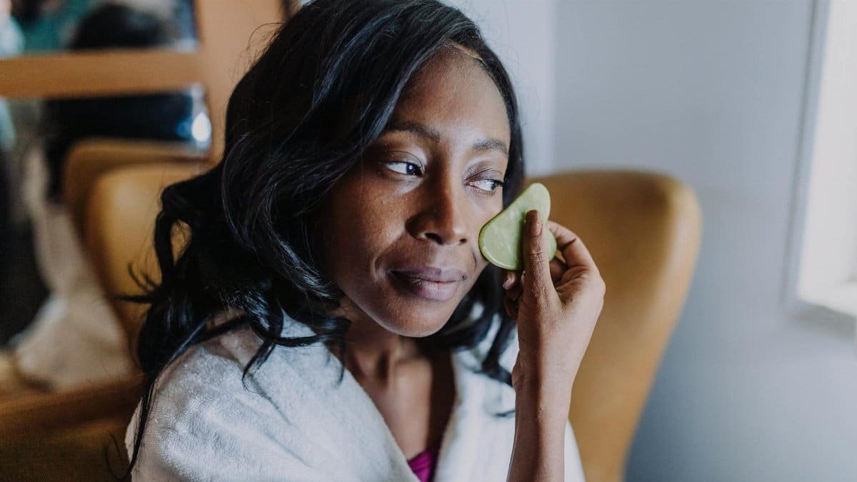 African American woman in spa robe applying cucumber to face, embodying relaxation and self-care.