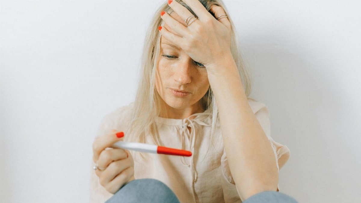 A concerned woman looks at a pregnancy test, reflecting emotions of anxiety and uncertainty.