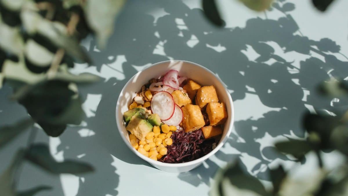 Top view of a vibrant poke bowl with tofu, avocado, and vegetables, surrounded by natural shadows.
