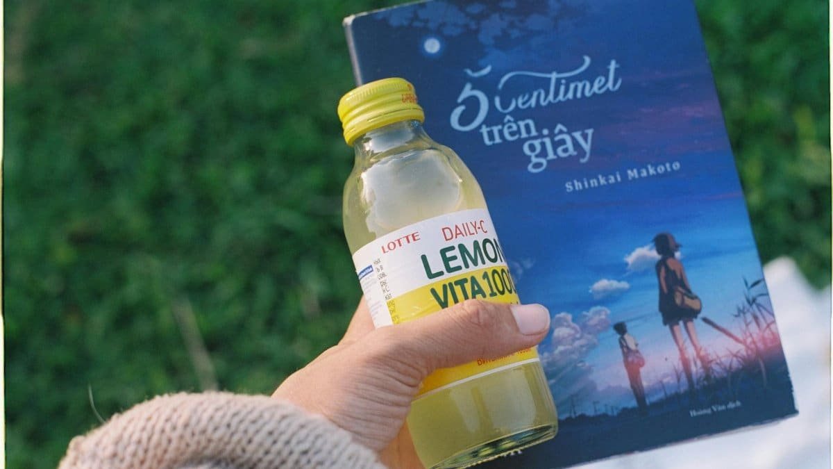 A person holding a bottle of lemon drink and a book outdoors, capturing a relaxing moment in nature.