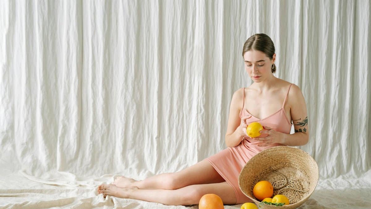 A peaceful woman in a pink dress holds a lemon, surrounded by citrus fruits, creating a refreshing mood.