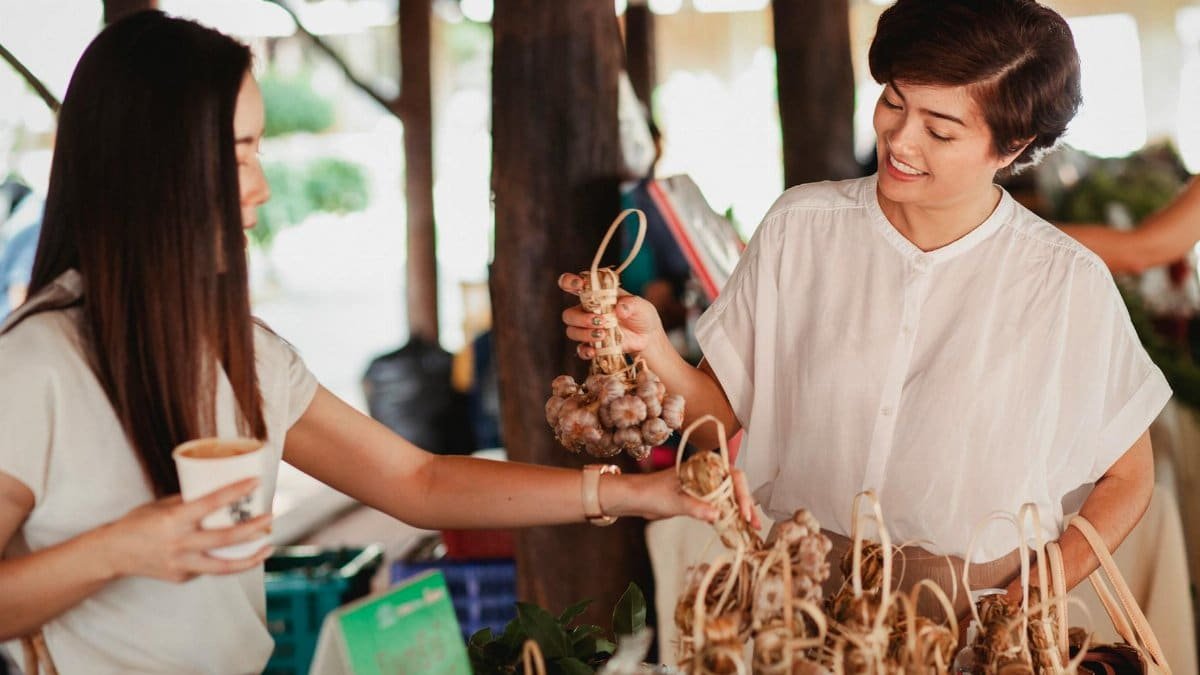 Two women happily exchanging goods and coffee at a local market.