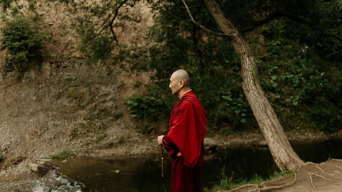 A Buddhist monk in meditation by a tranquil waterfall, symbolizing peace and spirituality.