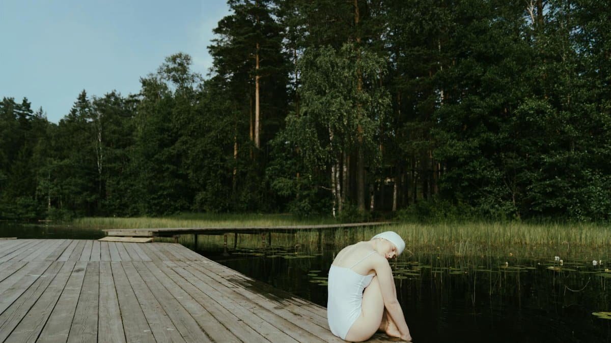 Woman relaxing on a lakeside wooden dock surrounded by lush greenery, embracing tranquility.