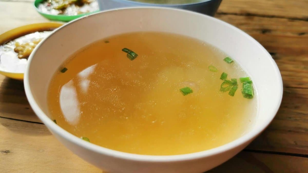 Delicious homemade soup garnished with scallions in a bowl on a rustic wooden table.