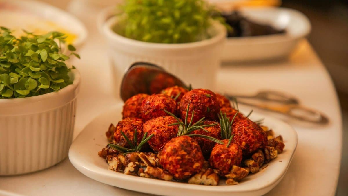 Close-up of spicy cheese balls garnished with rosemary and nuts, surrounded by fresh herbs.