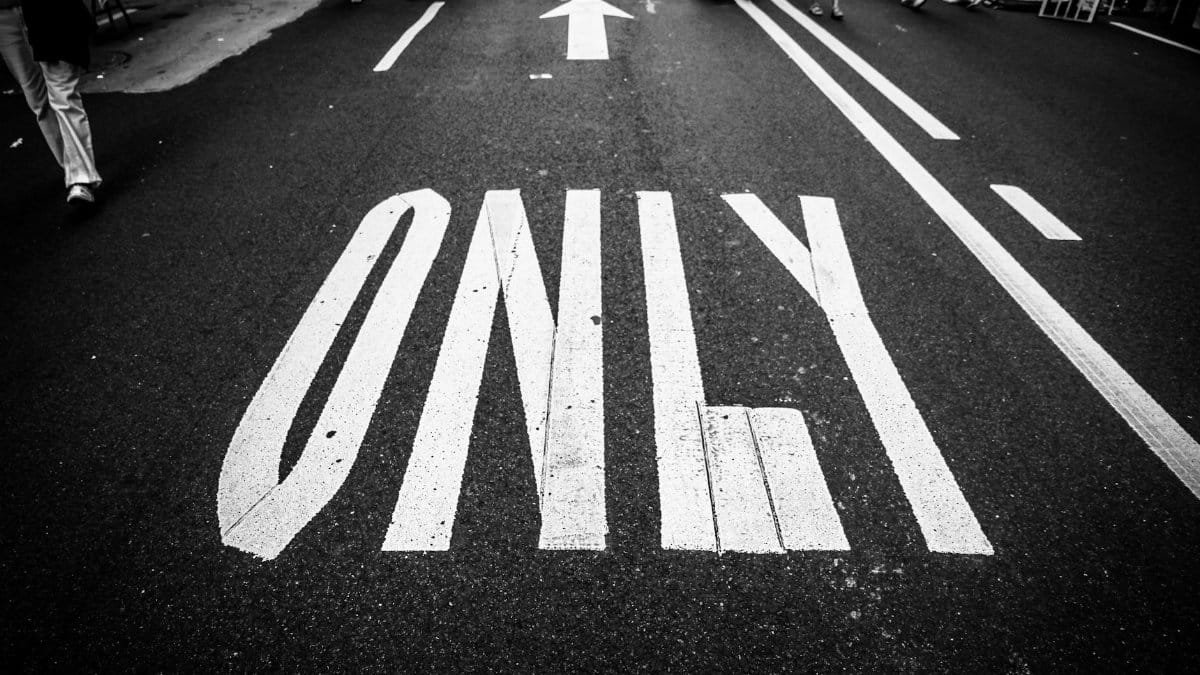 Black and white photo of road, showing traffic markings, a crowd, and an arrow.