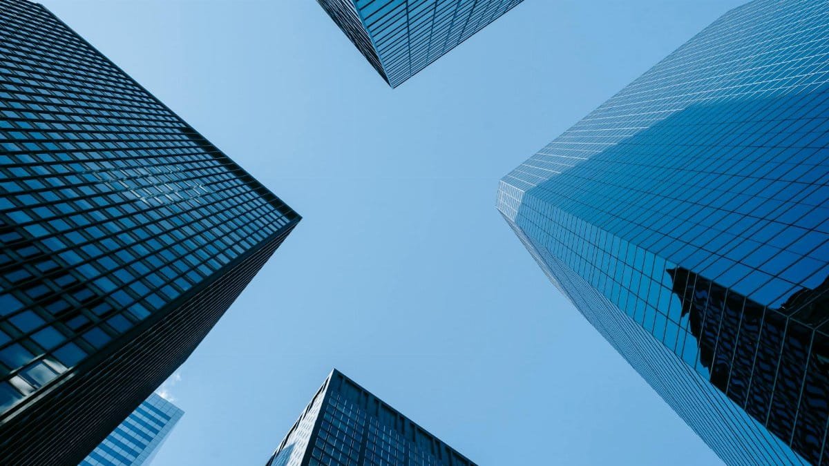 Low angle of high business towers with glass mirrored windows located in megalopolis downtown against blue sky