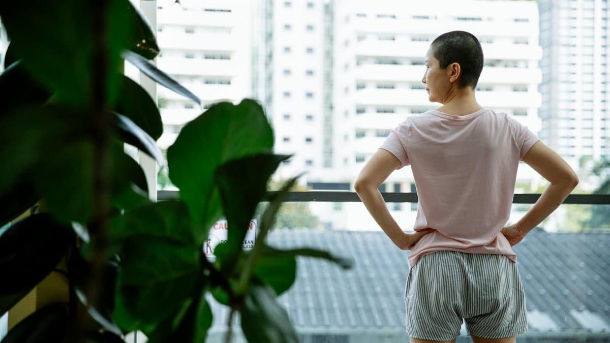 Back view of ethnic ill female with hands on waist looking away on balcony of hospital