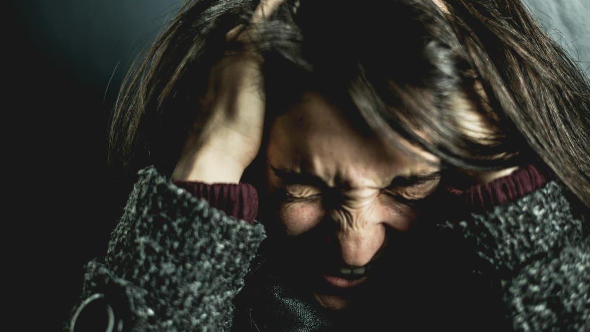 Close-up of a woman in distress with eyes closed and hands in hair, expressing anxiety.