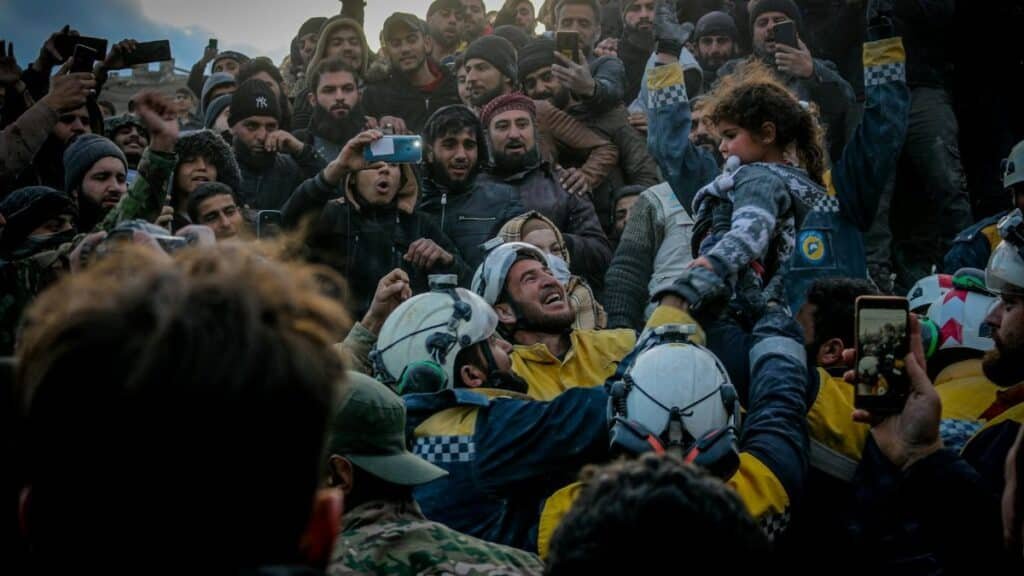 Rescue workers celebrate saving a child in Idlib, Syria amid a supportive crowd.