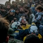 Rescue workers celebrate saving a child in Idlib, Syria amid a supportive crowd.