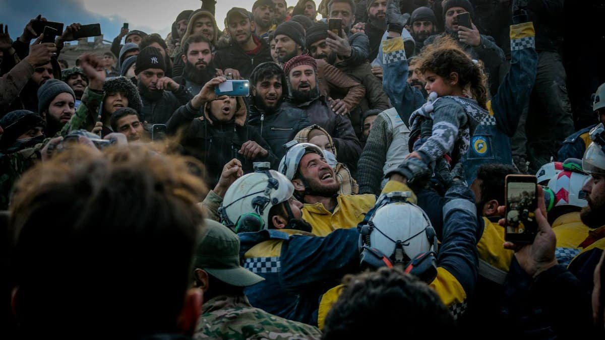 Rescue workers celebrate saving a child in Idlib, Syria amid a supportive crowd.