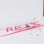 Close-up of a red pencil writing 'stress' on paper, symbolizing pressure and creativity.
