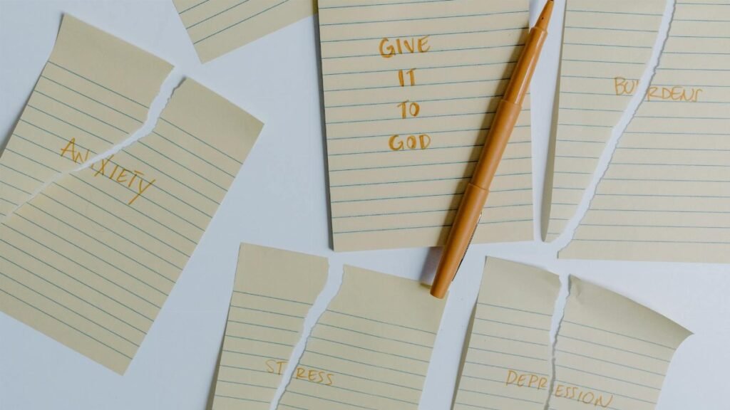 Ripped notebook pages with words anxiety, stress, depression, give it to God and a pen on a table.