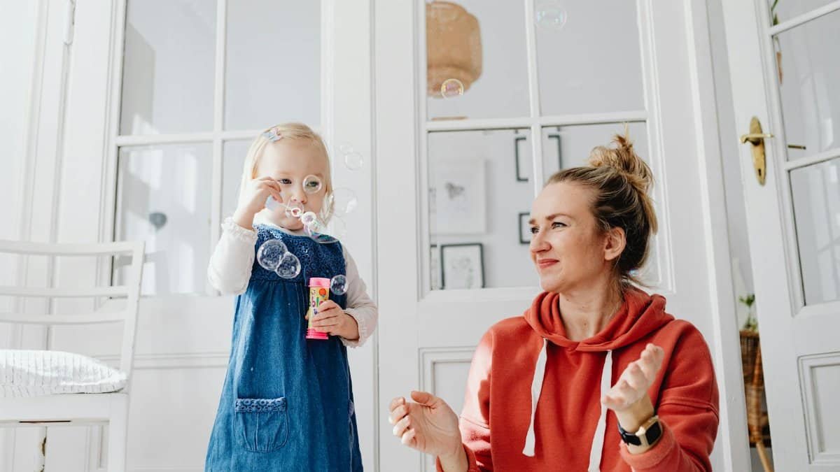 A joyful moment of a mother and daughter playing with bubbles indoors.