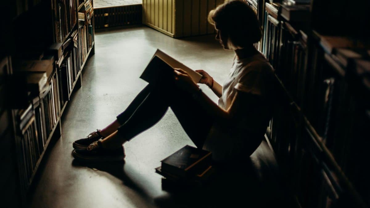A young woman engrossed in a book, sitting on the floor of a quiet library, creating a cozy reading atmosphere.