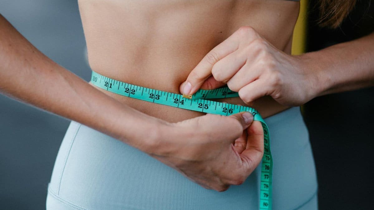 Close-up of a woman measuring her waist with a tape, representing fitness, health, and weight loss.