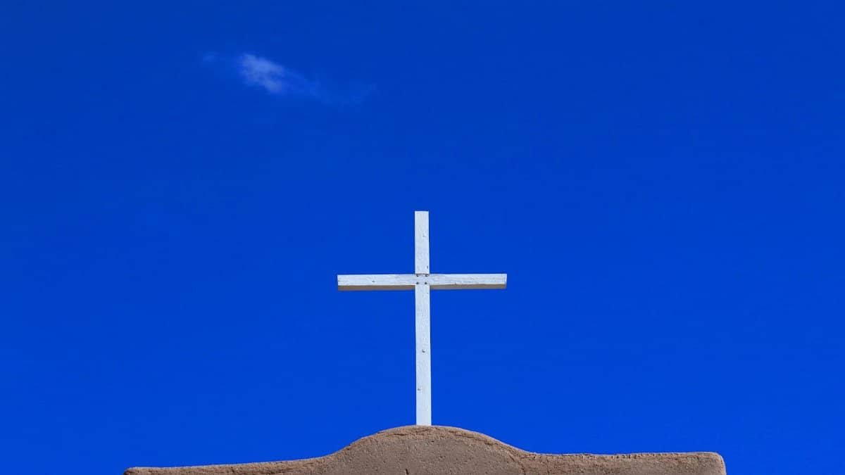 A white cross on adobe building at Santa Fe, NM, silhouetted against a clear blue sky.