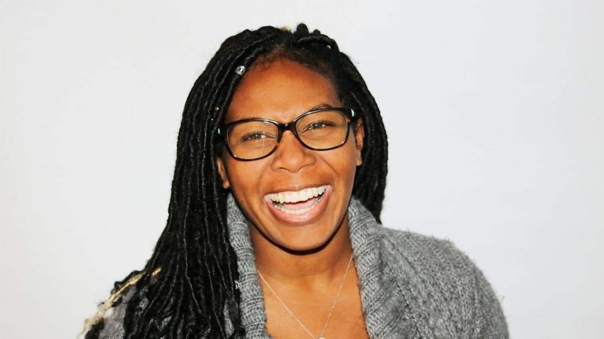 A vibrant portrait of a smiling woman with dreadlocks and glasses, exuding joy.