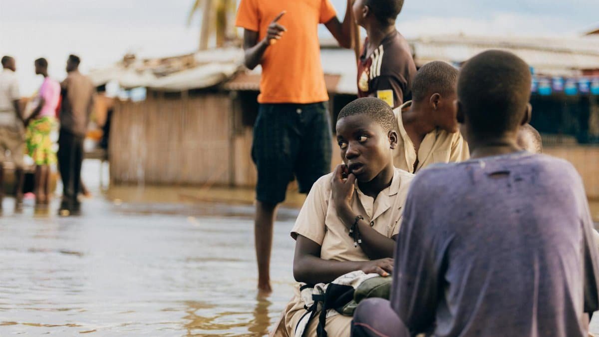 Children in rural village navigate flood waters, depicting resilience.