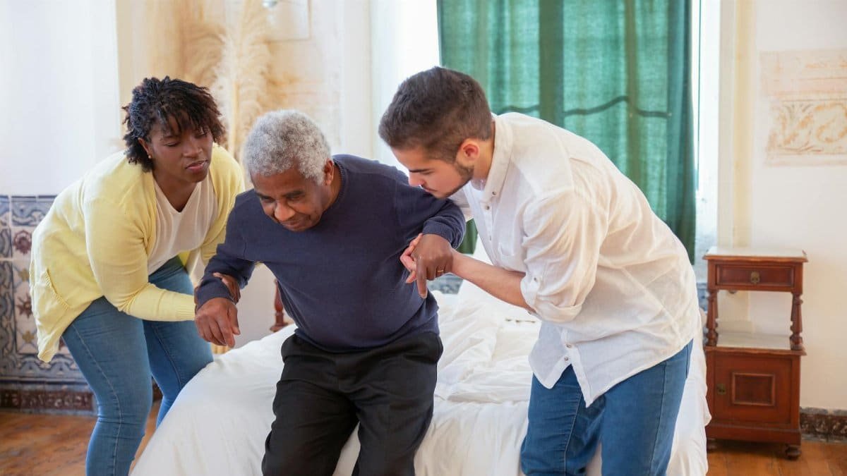 An elderly man receiving assistance from caregivers in a cozy home environment.