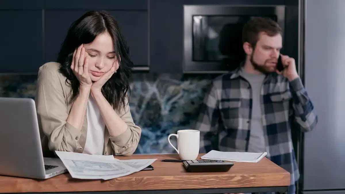 A couple dealing with financial stress, surrounded by bills and a laptop indoors.