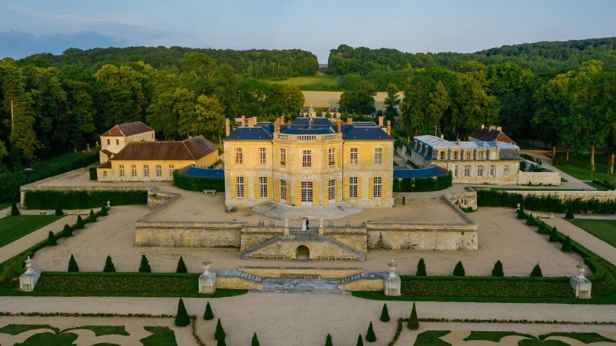 Elegant aerial view of a historic French château surrounded by lush gardens and trees, in summer.