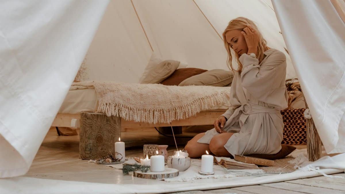 A woman enjoys a peaceful glamping moment, surrounded by candles in a cozy tent.