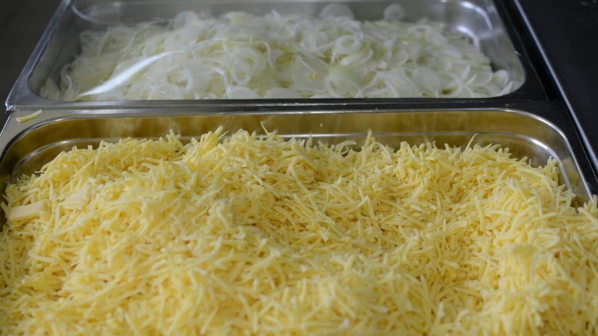 Close-up of shredded cheese and sliced onions in metal trays, perfect for cooking or catering setups.