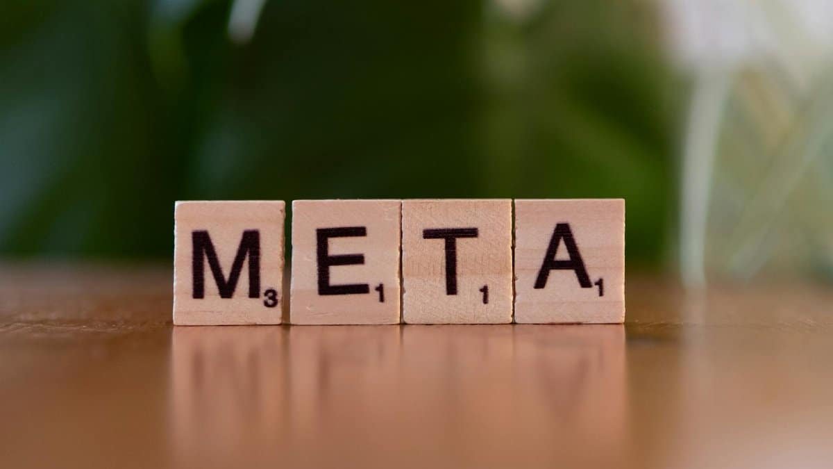 Wooden letter blocks spell META on a table with a blurred green background.